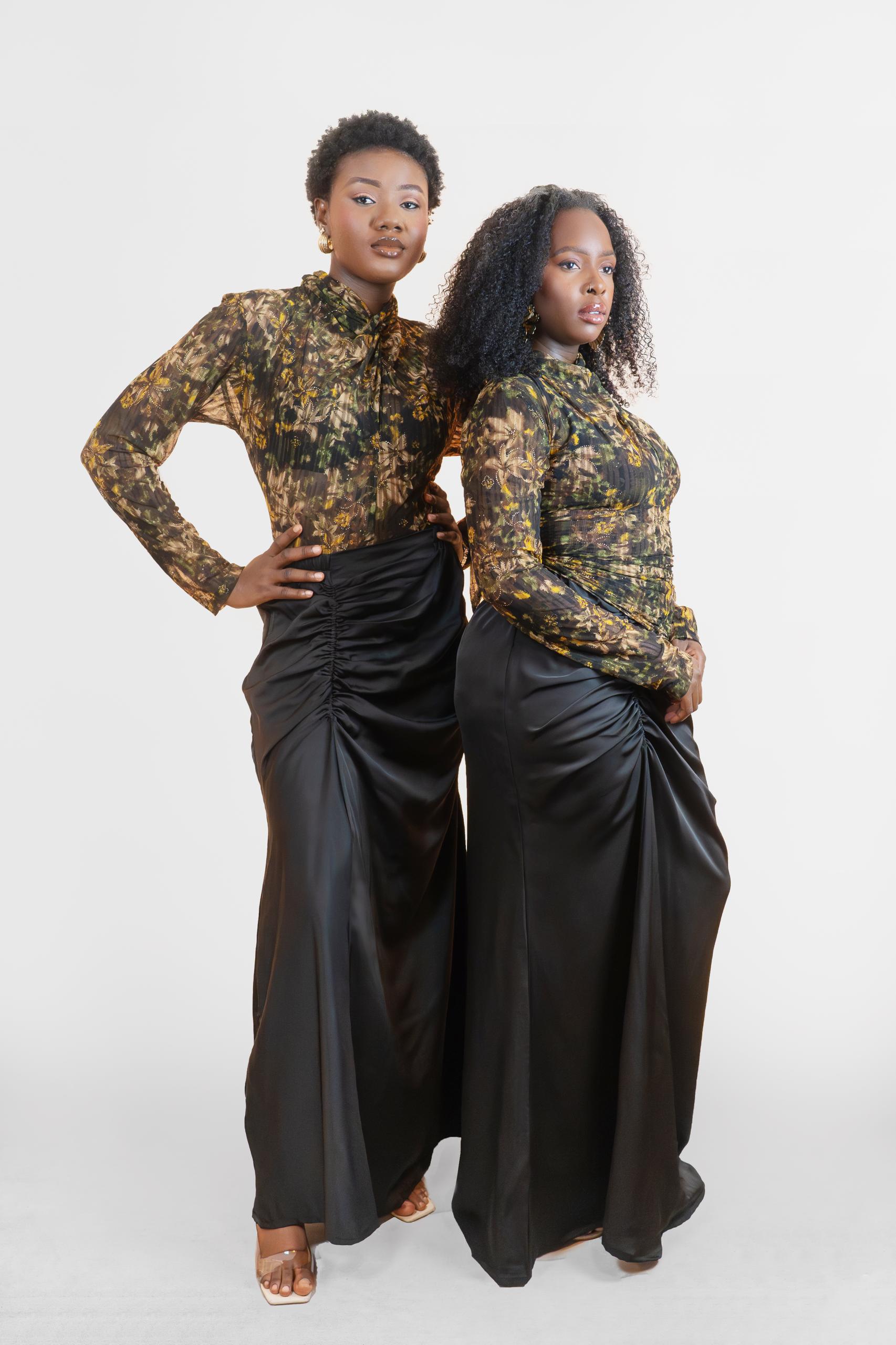 Two women wearing matching outfits with a floral top and black pants on a white background